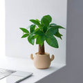 Kunstig grønn plante i dekorativ figurpotte